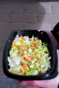 A hand holding a taco bell veggie power bowl with lettuce, cheese, and tomatoes.