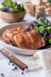 Broiled bone-in pork chops on a plate with a side of salad greens. In the back are bowls of salad greens and bread slices and salt and pepper shakers.