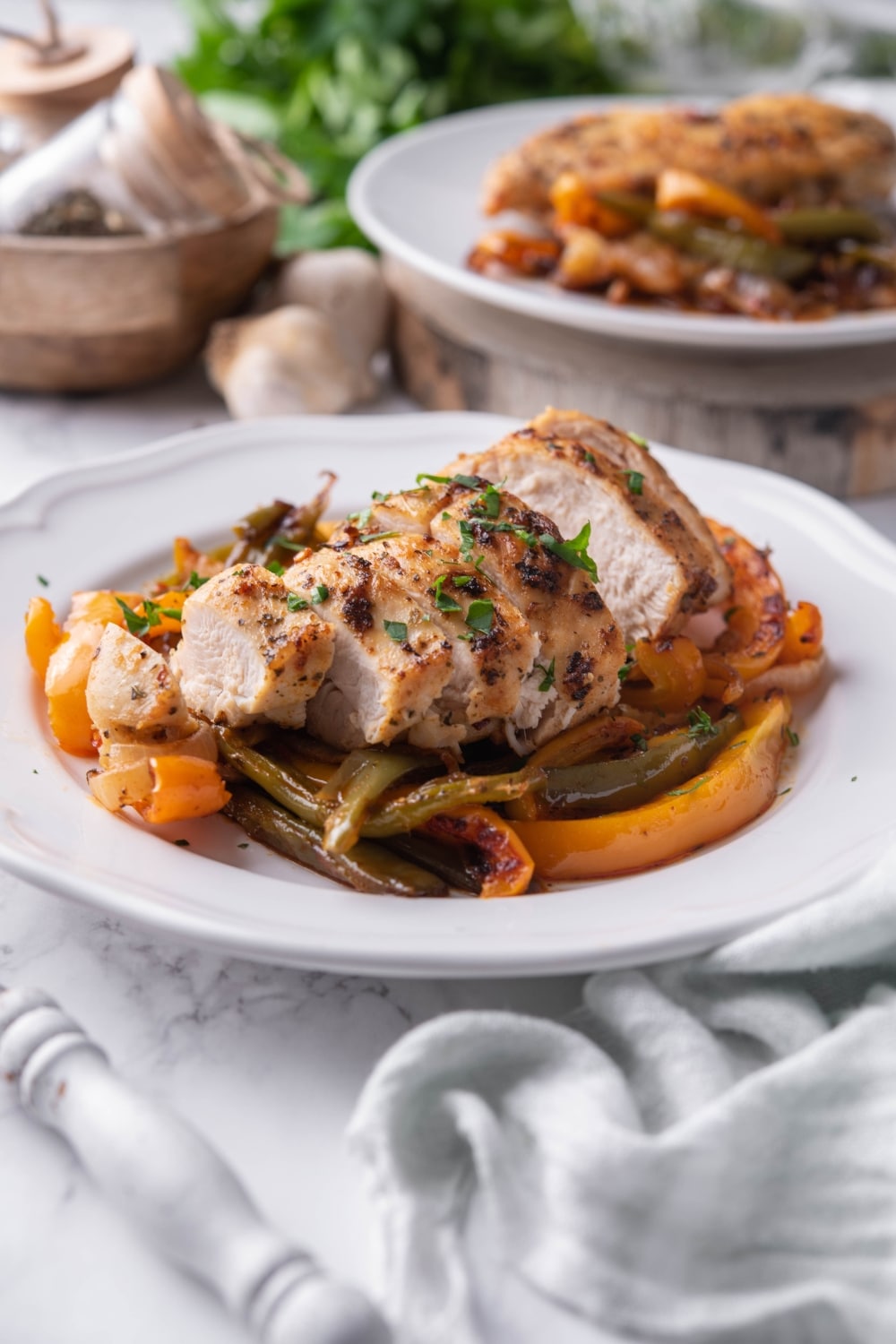 Sliced chicken breast over peppers on a white plate with a fork. Behind is a second plate of chicken and peppers.