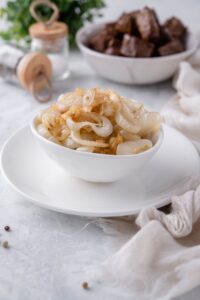 Sauteed onions in a white bowl on a white plate.