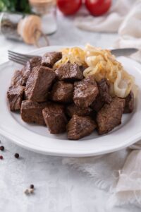 Steak tips served with caramelized onions on a white plate with a fork.