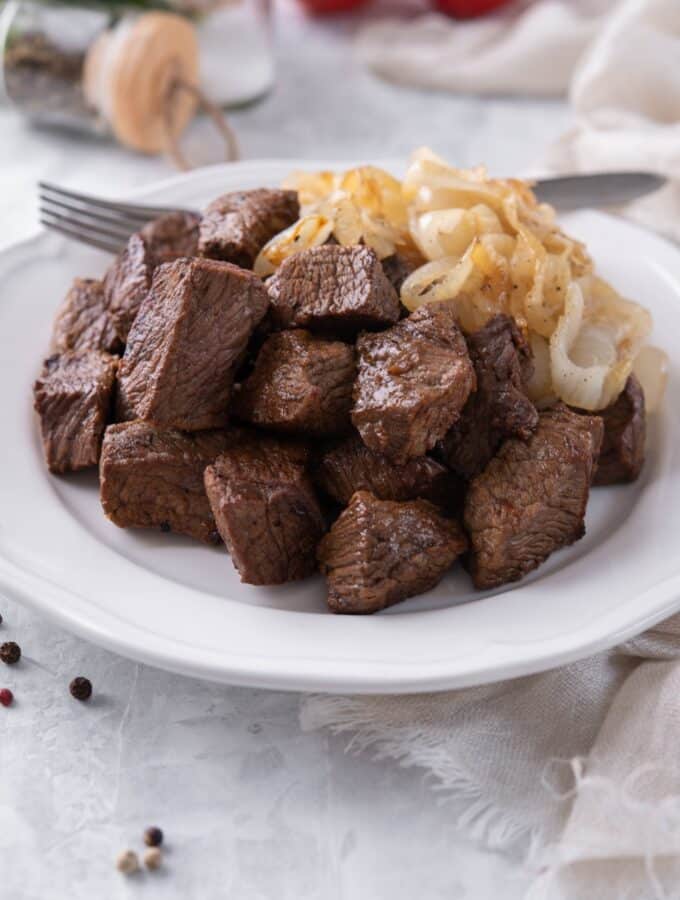 Steak tips served with caramelized onions on a white plate with a fork.