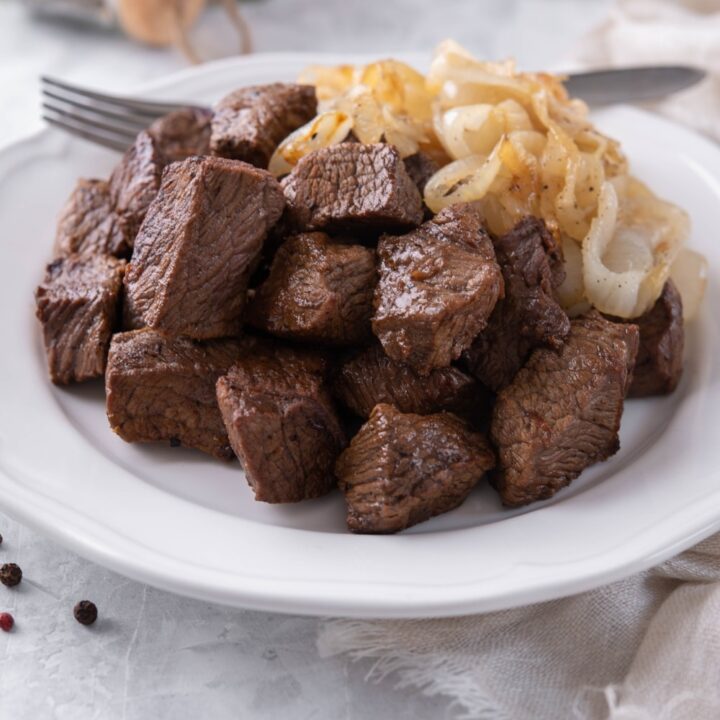 Steak tips served with caramelized onions on a white plate with a fork.