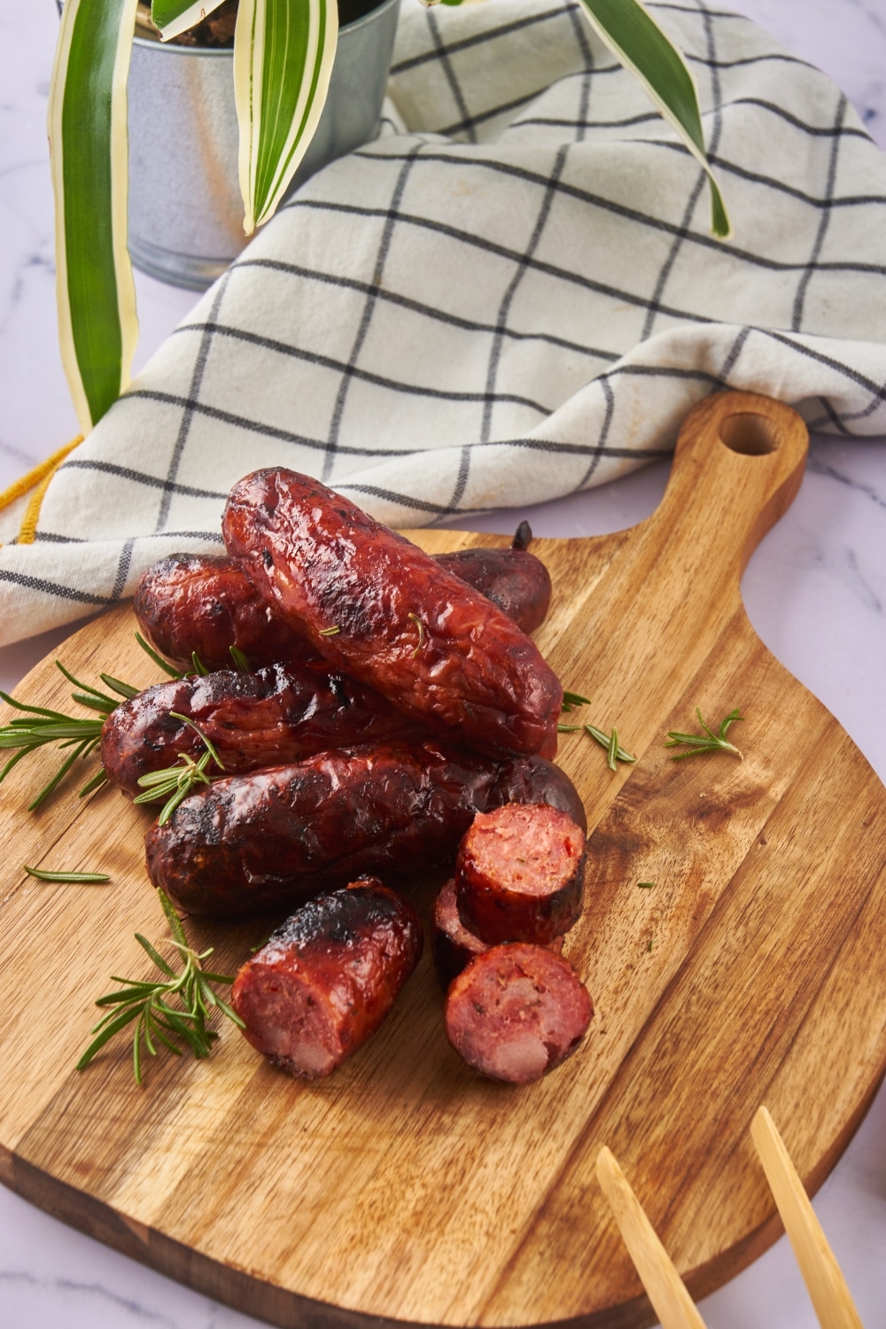 Oven roasted sausages on a wooden serving board. One of the sausages is sliced and a pair of wooden tongs is resting on the board.