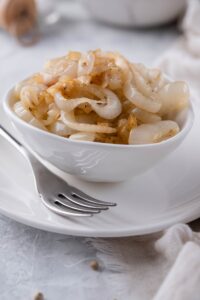 Sauteed onion rings in a white bowl on a white plate with a fork.