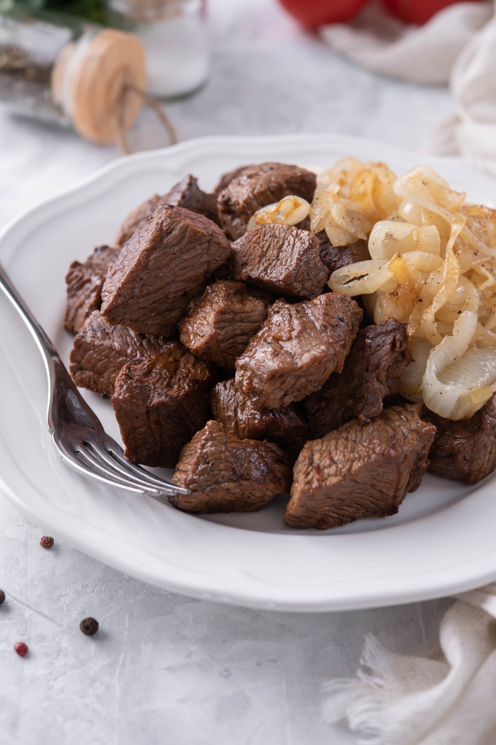 A closer look at seared steak tips on a plate. They're served with caramelized onions and a fork.