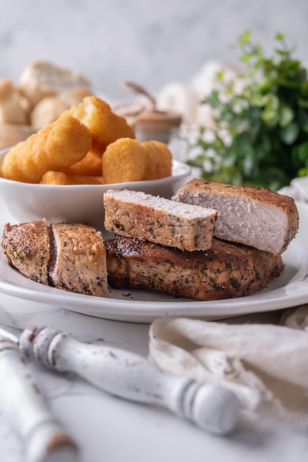 Thick cut pork chops with a side of tater tots on a white plate.