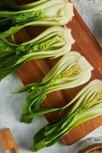 Four bok choy halves on a wooden cutting board.