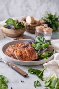 Two broiled bone-in pork chops with salad greens, served with bowls of salad greens and bread slices.