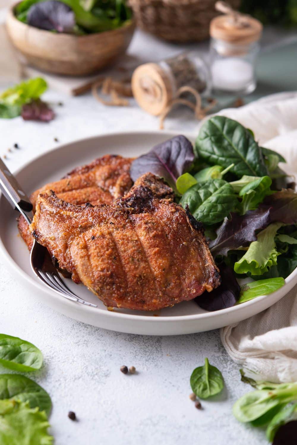 Two broiled bone-in pork chops on a plate with a side of salad greens.