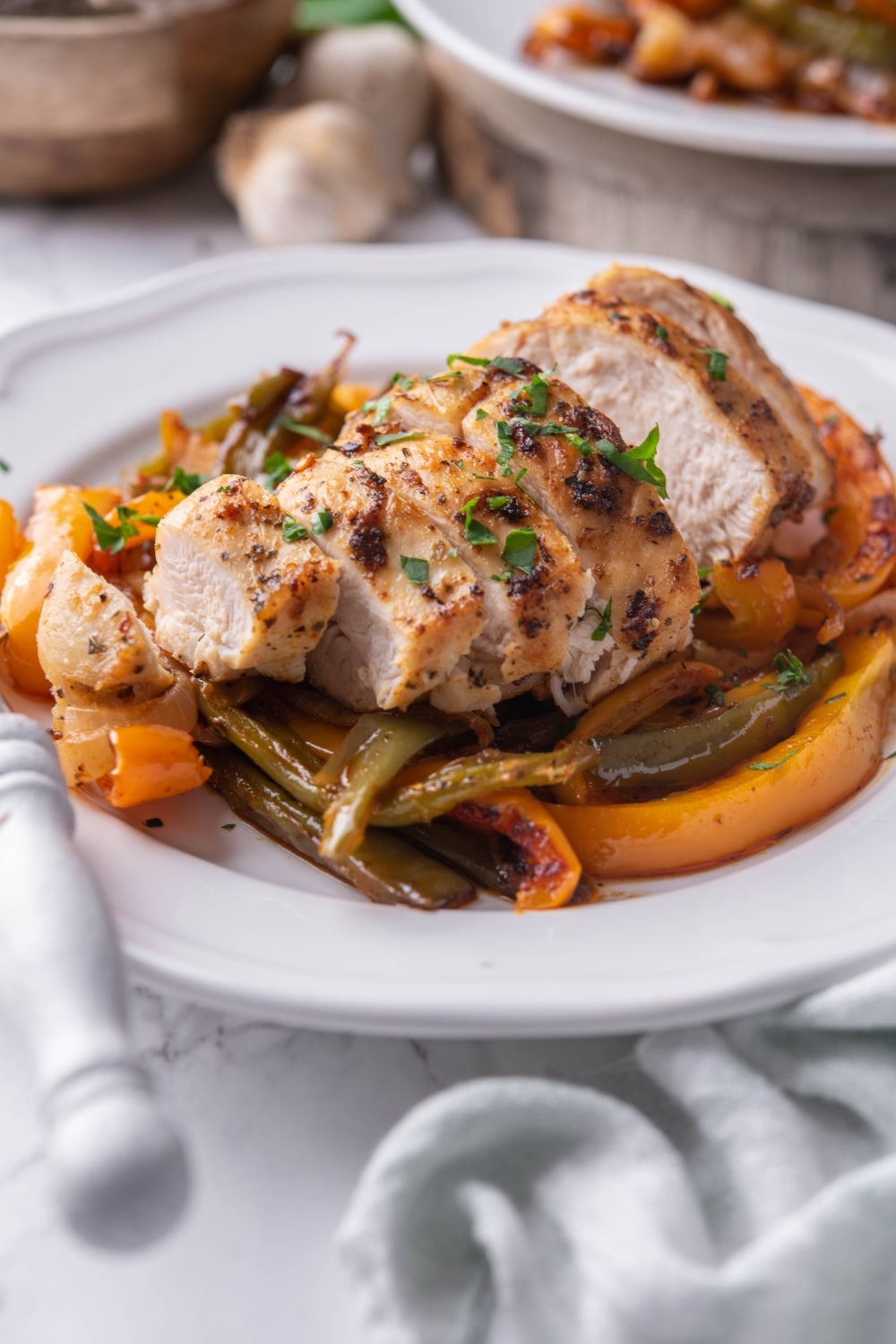 Sliced chicken breast over peppers on a white plate with a fork.