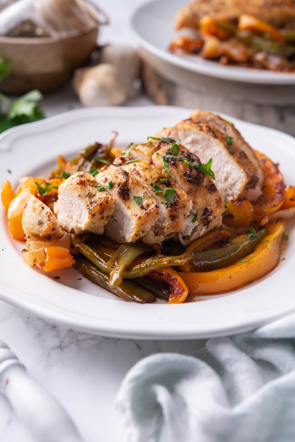 Sliced chicken breast over bell peppers on a white plate.