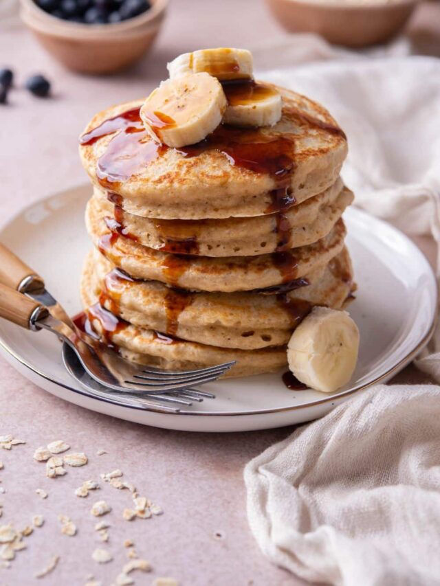 A stack of oat flour pancakes topped with banana slices and drizzled with date syrup on a plate with two forks.