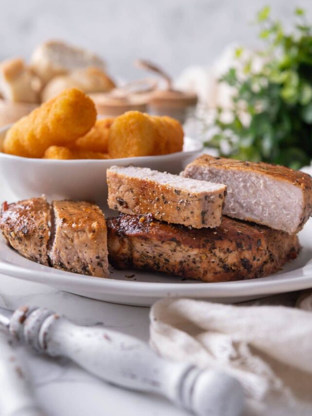 Two thick cut pork chops, one sliced into five pieces, on a white plate with a side of tater tots.