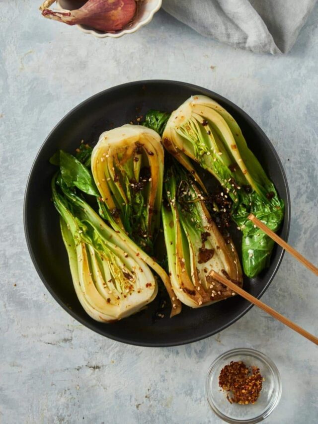 Four bok choy halves cooking in a skillet with red pepper flaked on top.