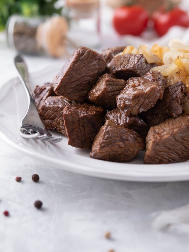 A plate of steak tips served with caramelized onions. A fork is resting on the plate.