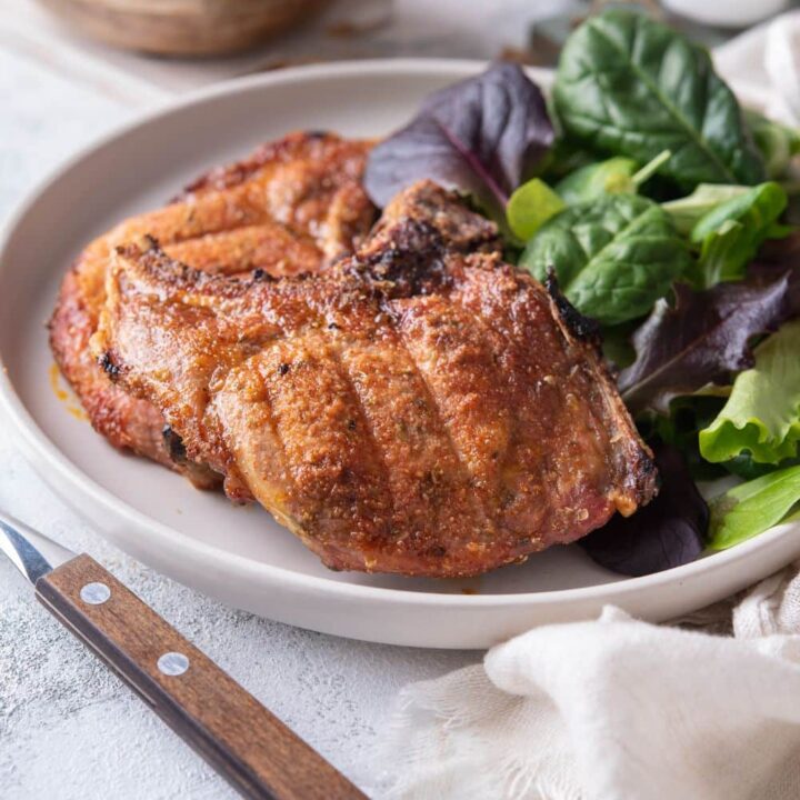 Two broiled bone-in pork chops with a side of salad greens on a plate.