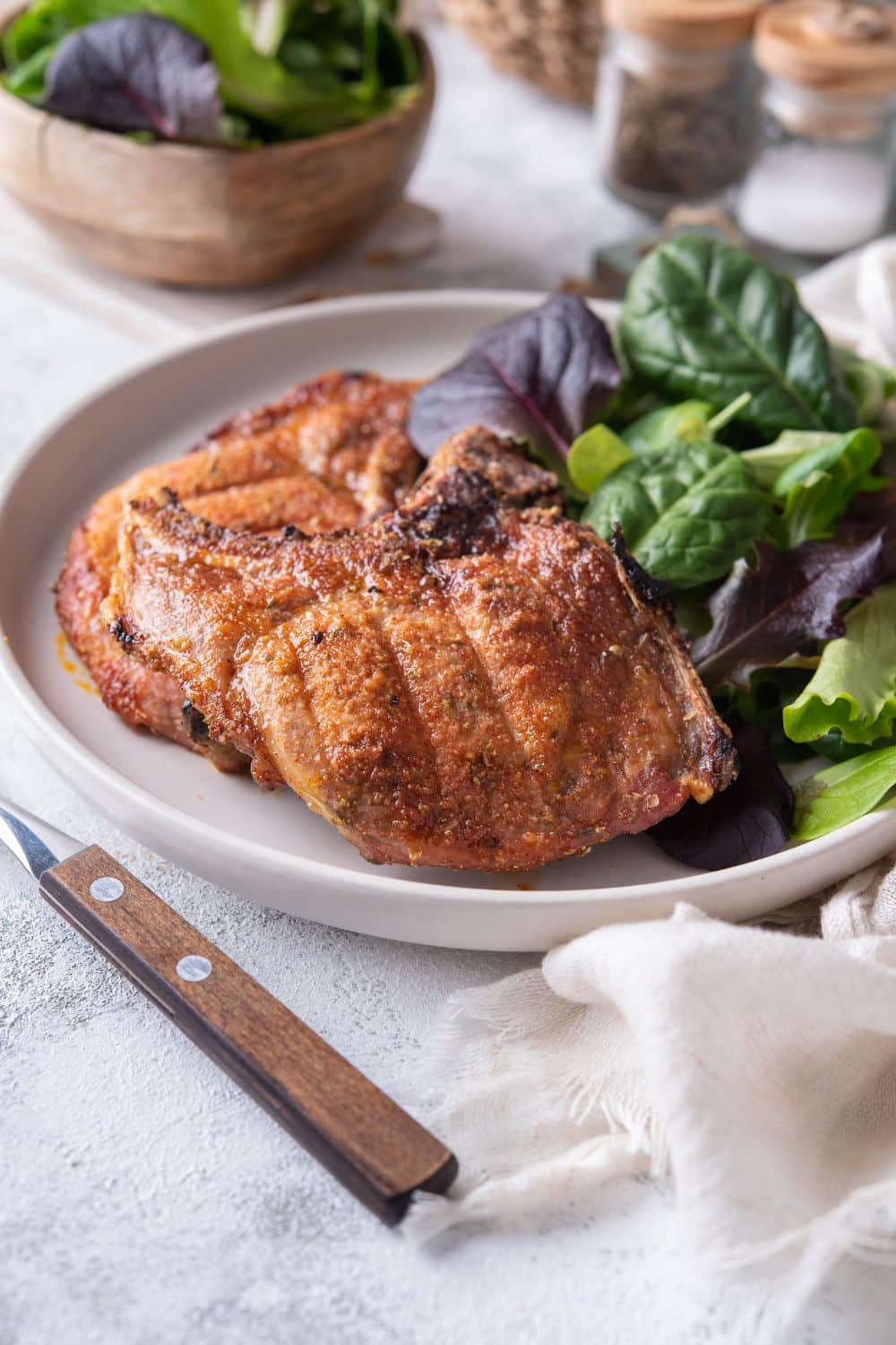 Two broiled bone-in pork chops with a side of salad greens on a plate.