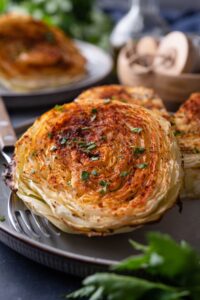 Two roasted cabbage steaks on a plate with a fork.