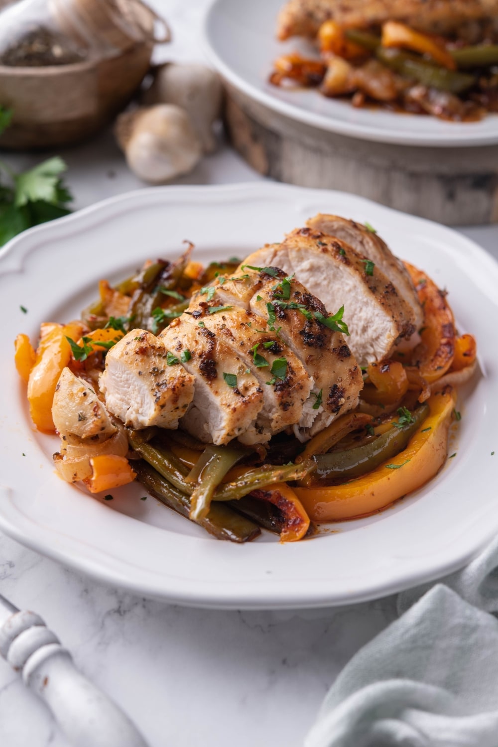 Sliced chicken breast and bell peppers garnished with fresh herbs on a white plate.