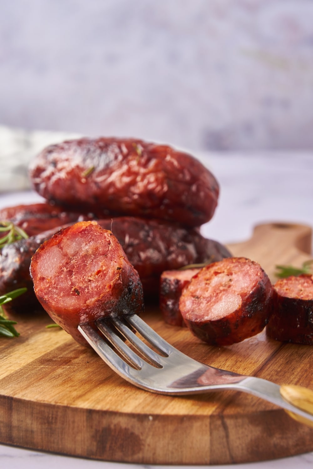 A piece of sliced oven roasted sausage on a fork. It's resting on a wooden serving board with more oven roasted sausages.