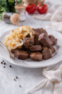 Steak tips and caramelized onions on a white plate with a fork.