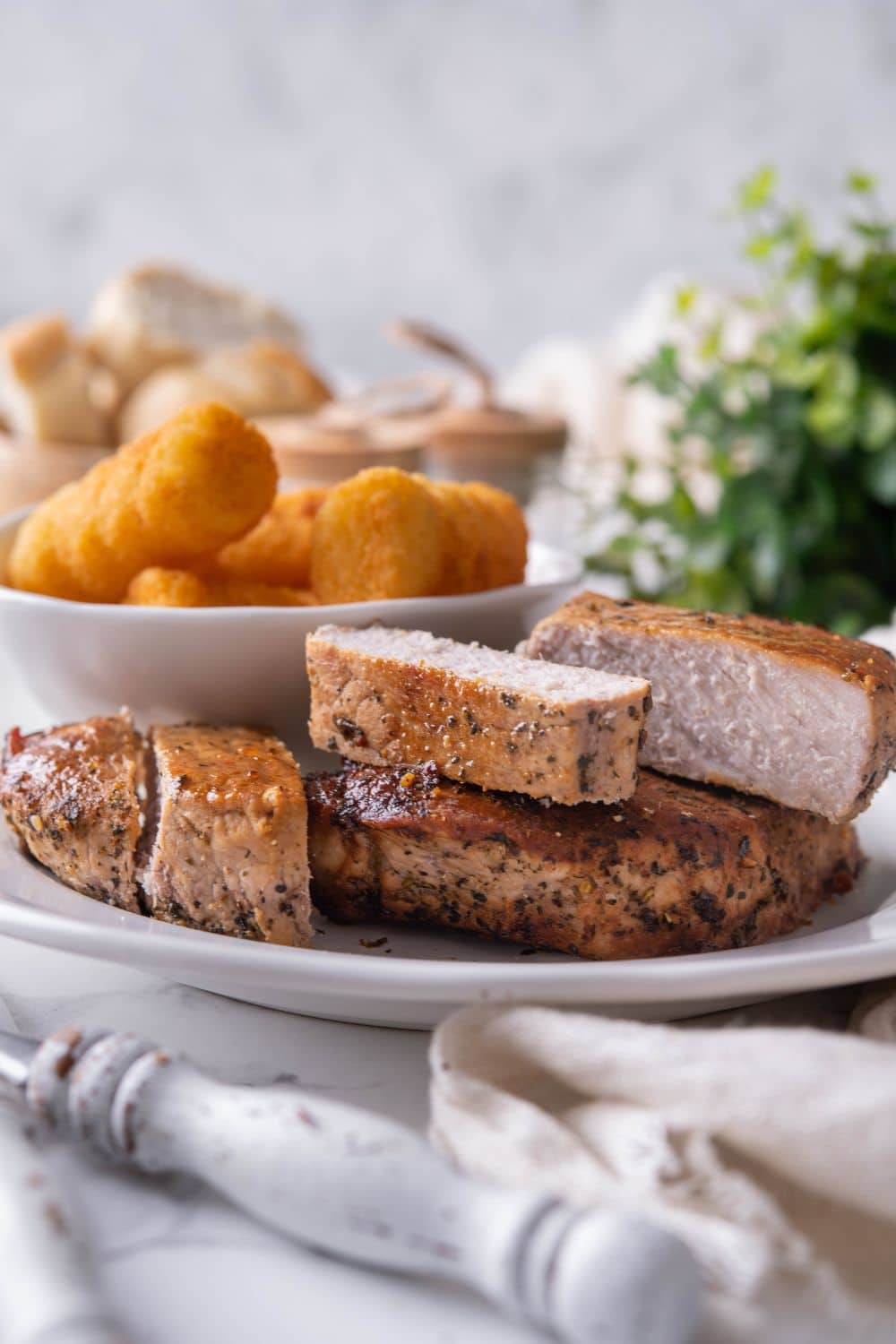 Two thick cut pork chops, one sliced into five pieces, on a white plate with a side of tater tots.