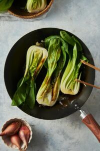 Three pieces of bok choy cooking in a skillet.