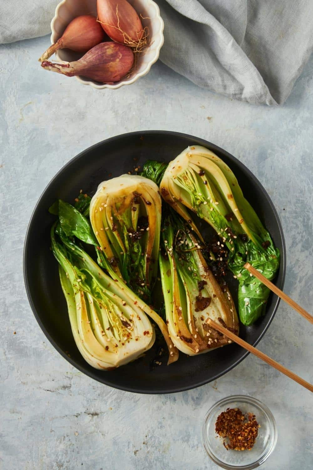 Four bok choy halves cooking in a skillet with red pepper flaked on top.