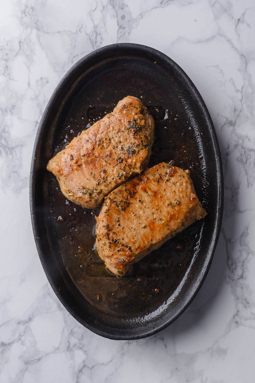 Two seared thick cut pork chops on a cast iron plate.