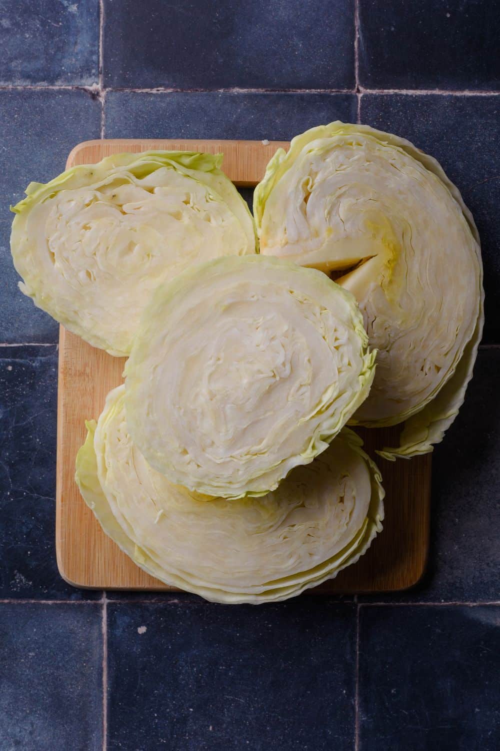 Uncooked cabbage sliced into four steaks on a wooden cutting board.