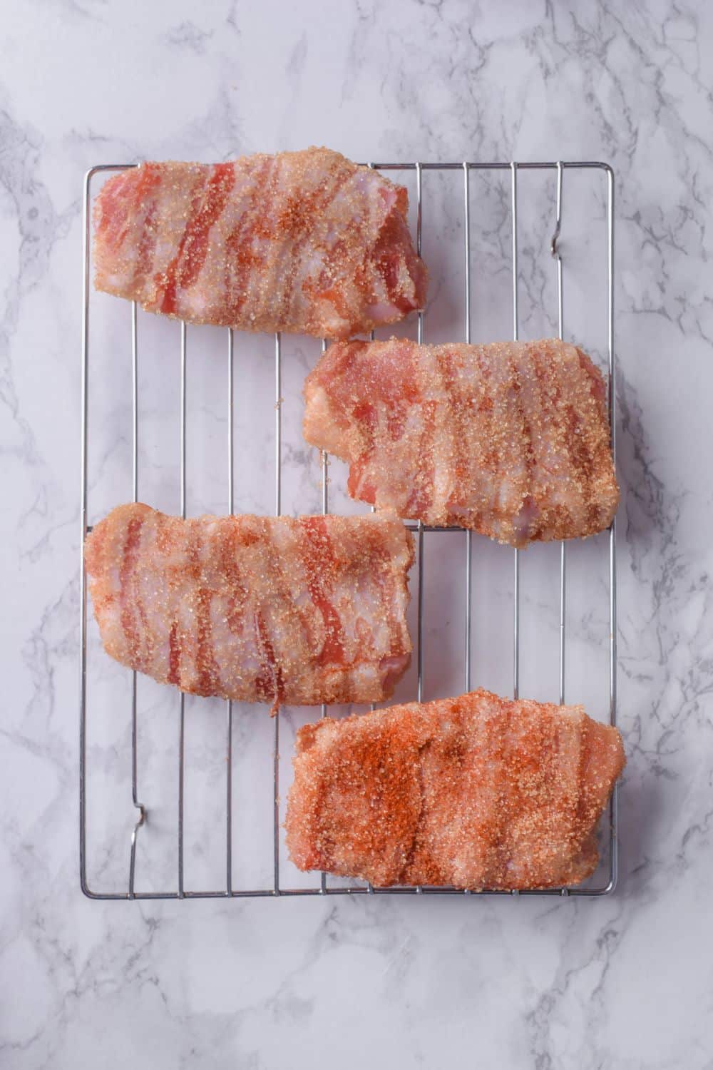 Four uncooked bacon wrapped pork chops rubbed with brown sugar and chili powder on a baking rack.