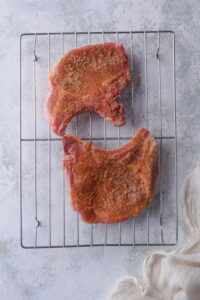 Two uncooked bone-in pork chops coated in spice rub on a baking tray.