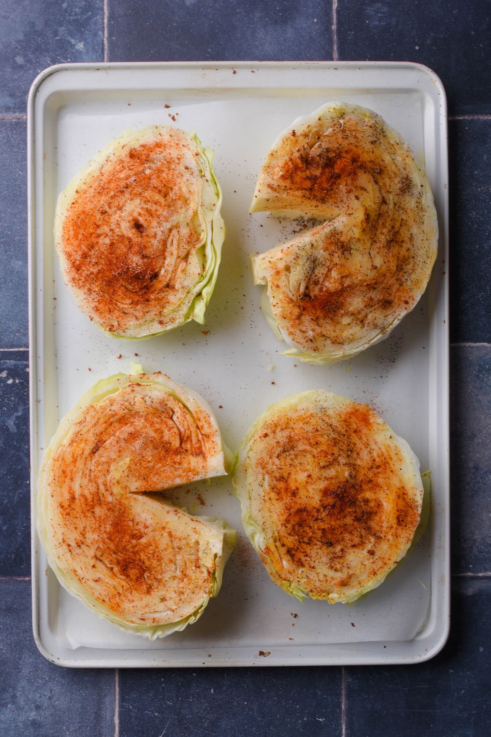 Four uncooked seasoned cabbage steaks on a tray.