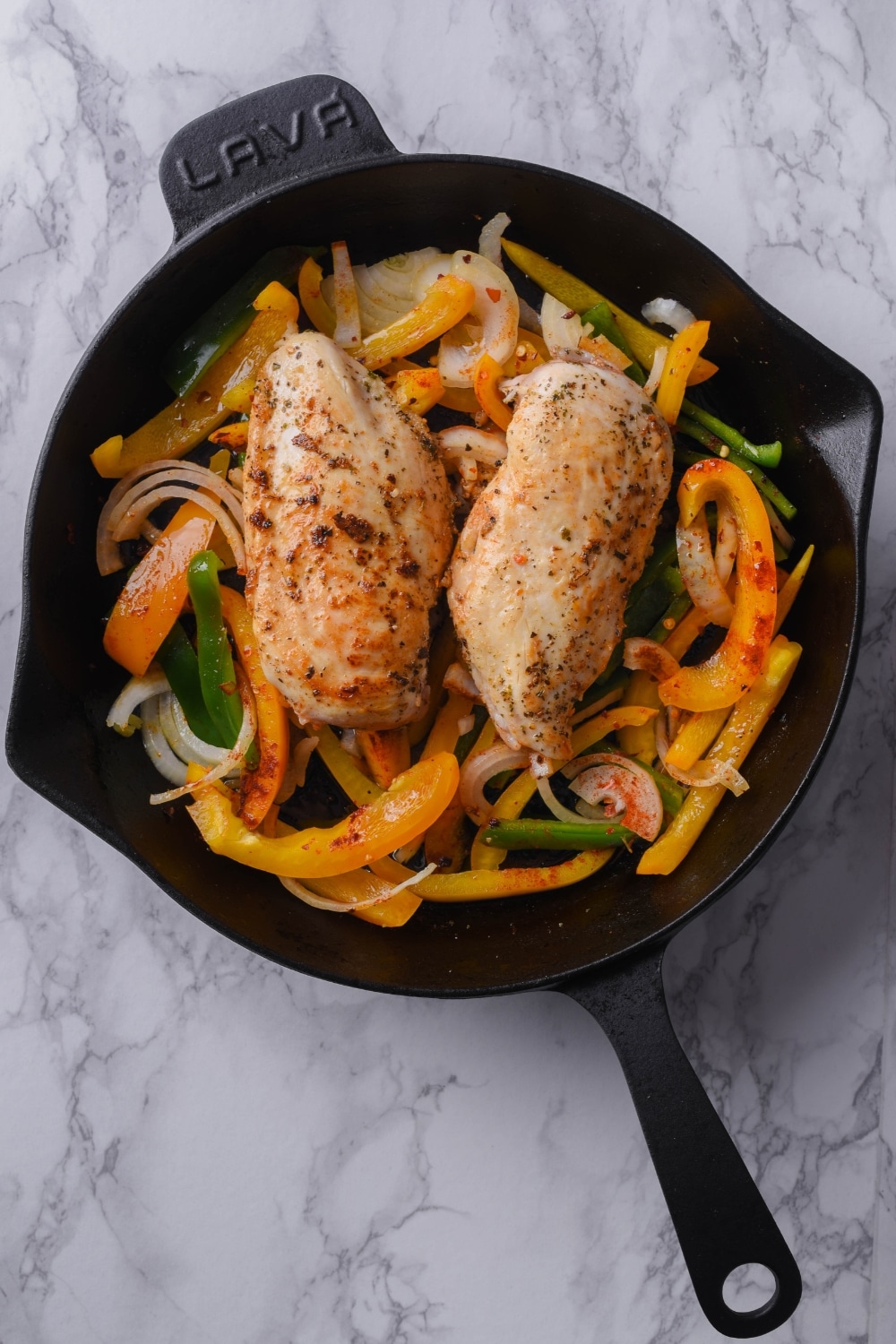 Seared seasoned chicken breasts over sliced bell pepers and onions in a cast iron skillet.