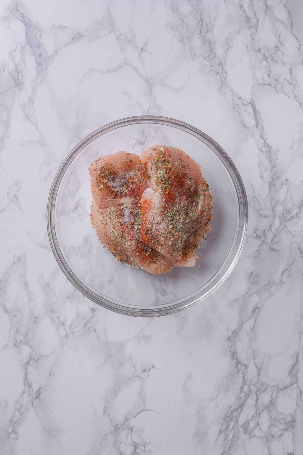 Raw seasoned chicken breast fillets in a glass bowl.