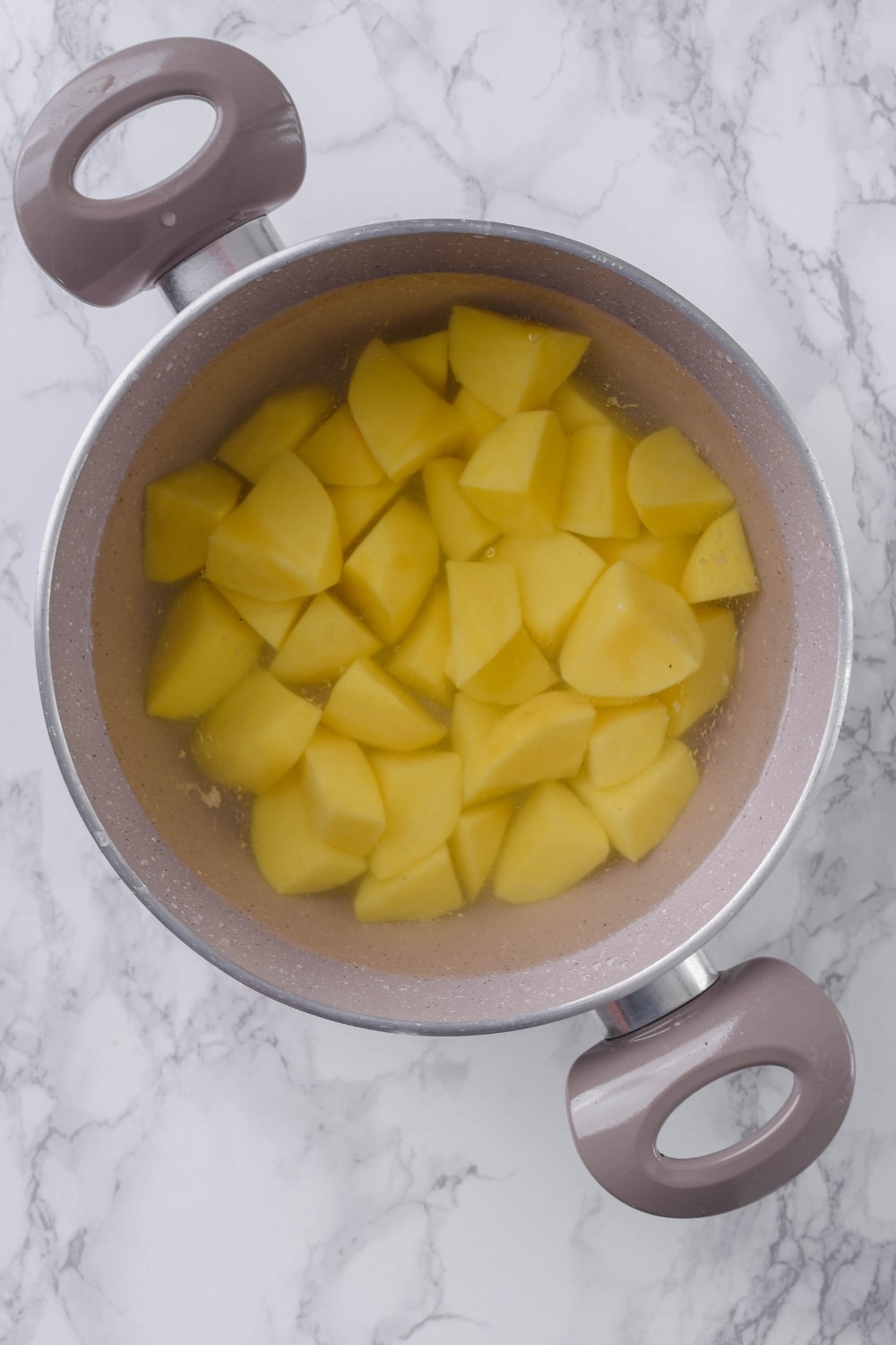 Chopped potatoes soaking in water in a large pot.