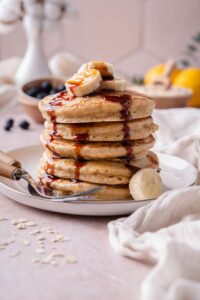 Oat flour pancakes topped with banana slices and date syrup on a plate with two forks.