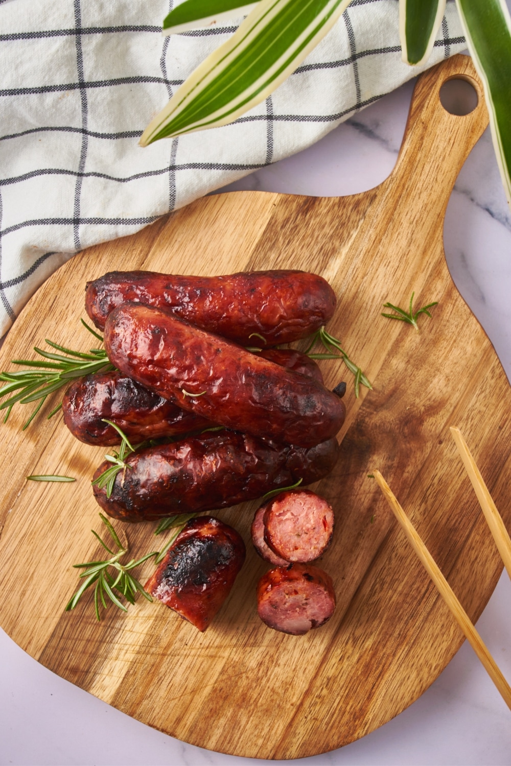 Oven cooked sausages, one sliced into bite-sized pieces, on a wooden serving board with a pair of wooden tongs.