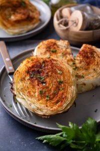 Roasted cabbage steaks on a plate with a fork, one with a slice taken out.
