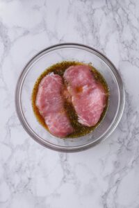 Two thick cut pork chops marinating in a glass bowl.