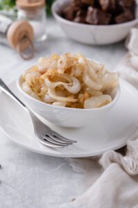 Sauteed onion rings in a white bowl, served on a white plate with a fork.