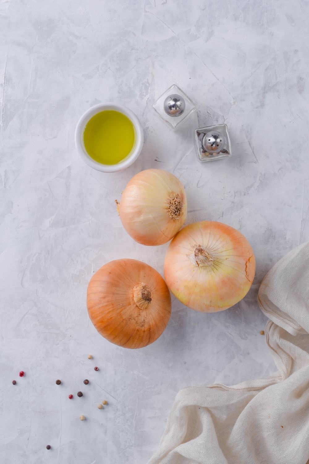 Three medium onions, a small bowl of oil, and salt and pepper shakers.