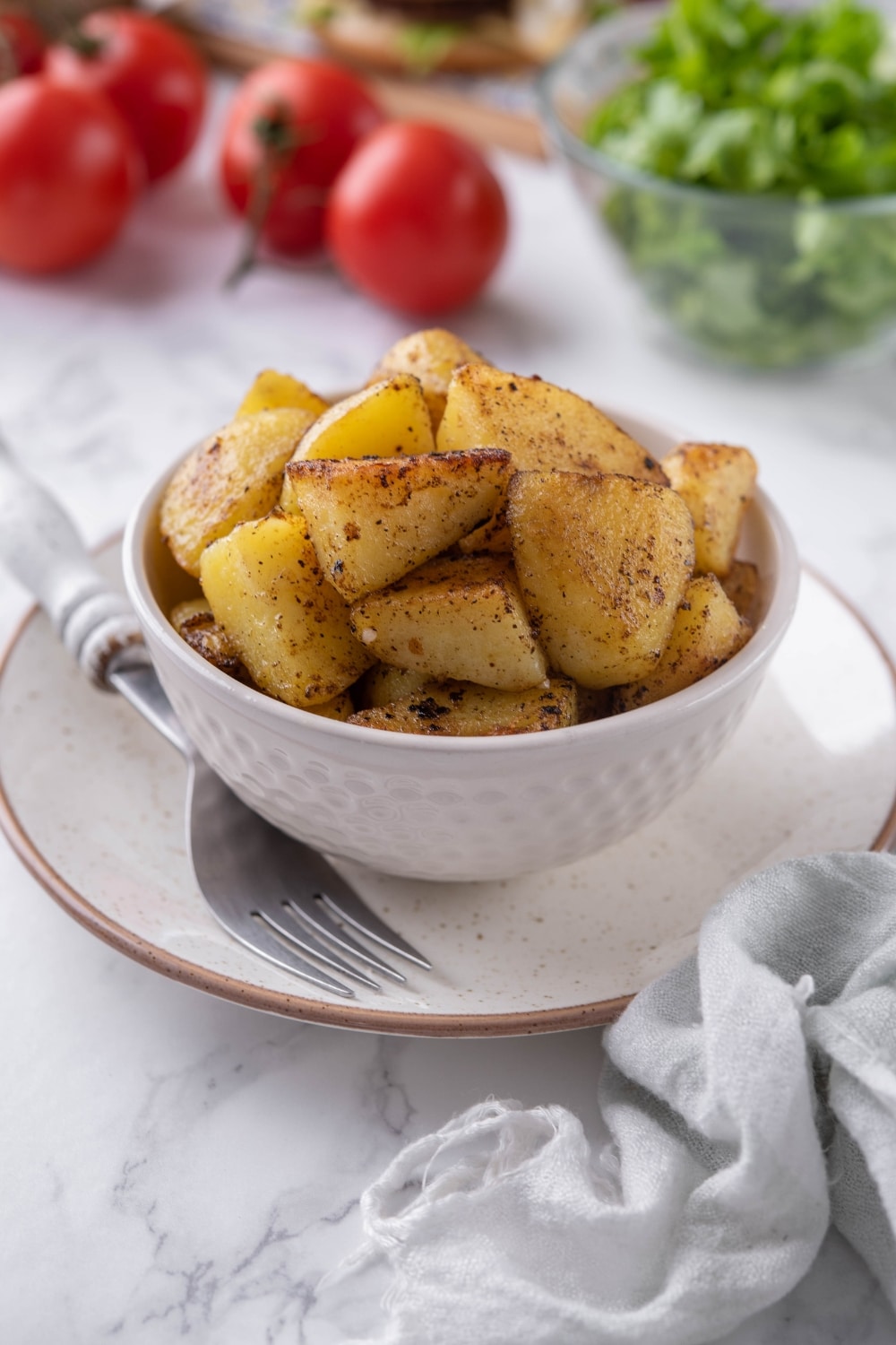 Sauteed potatoes in a white bowl, set on a plate with a fork.