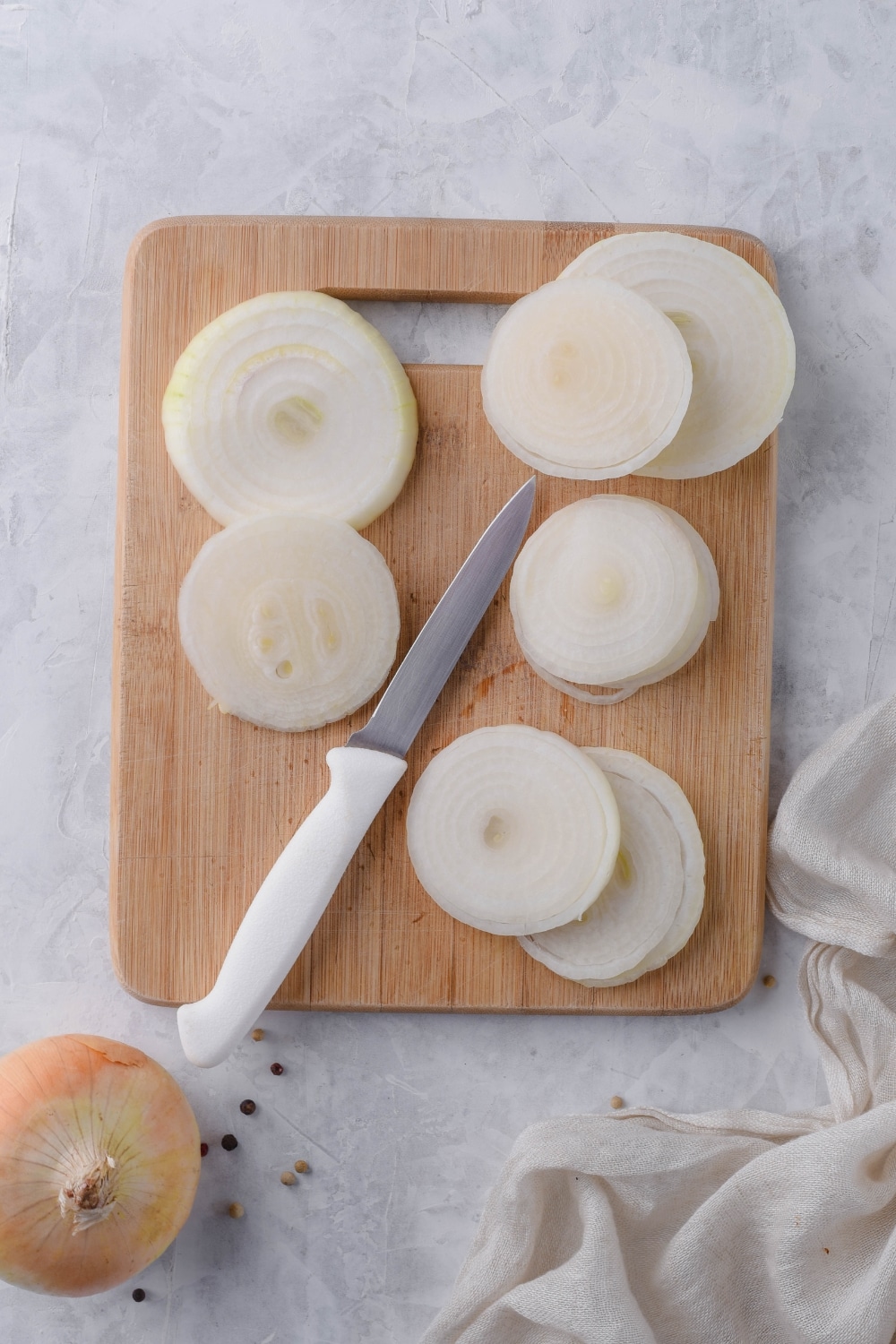 Raw onion slices on a wooden cutting board with a small knife.