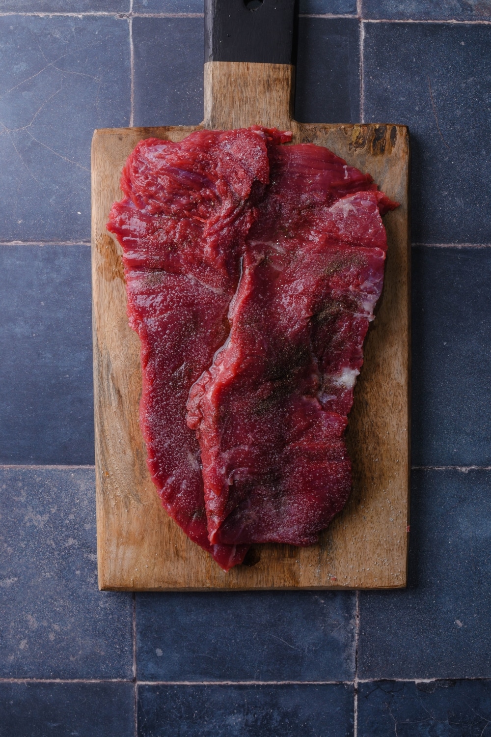 Raw skirt steak seasoned with salt and pepper on a wooden cutting board.