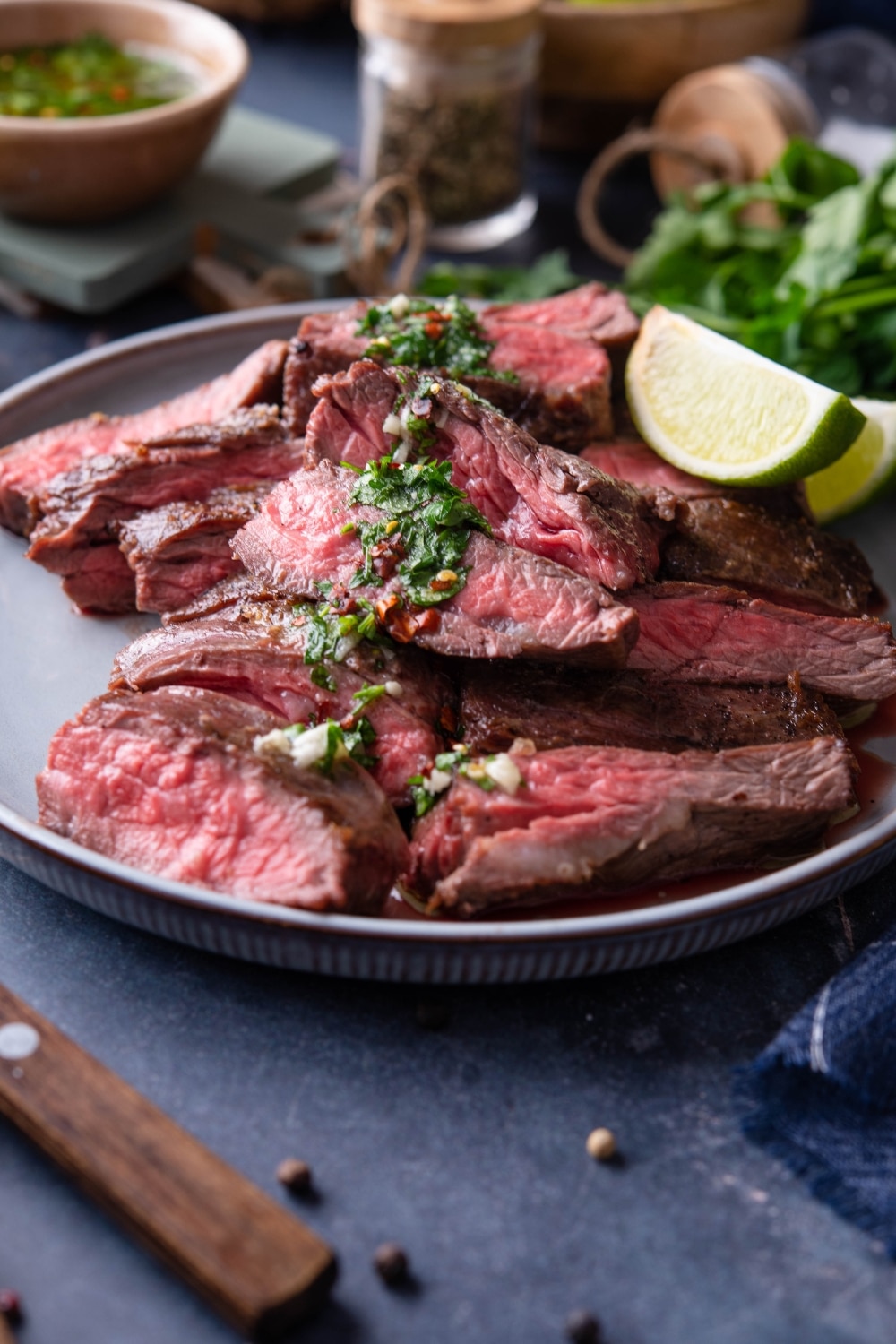 Medium rare skirt steak slices on a plate topped with chimichurri and served with lime wedges.