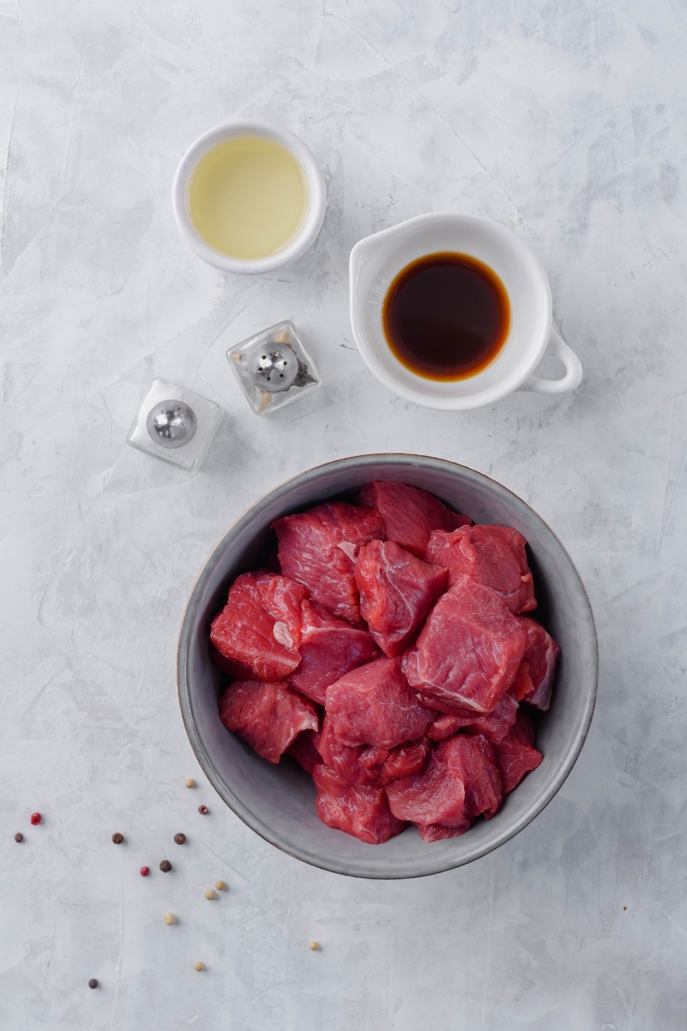 A bowl of raw steak tips, small bowls of oil and Worcestershire sauce, and salt and pepper shakers.