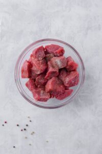 Raw seasoned steak tips in a glass bowl.