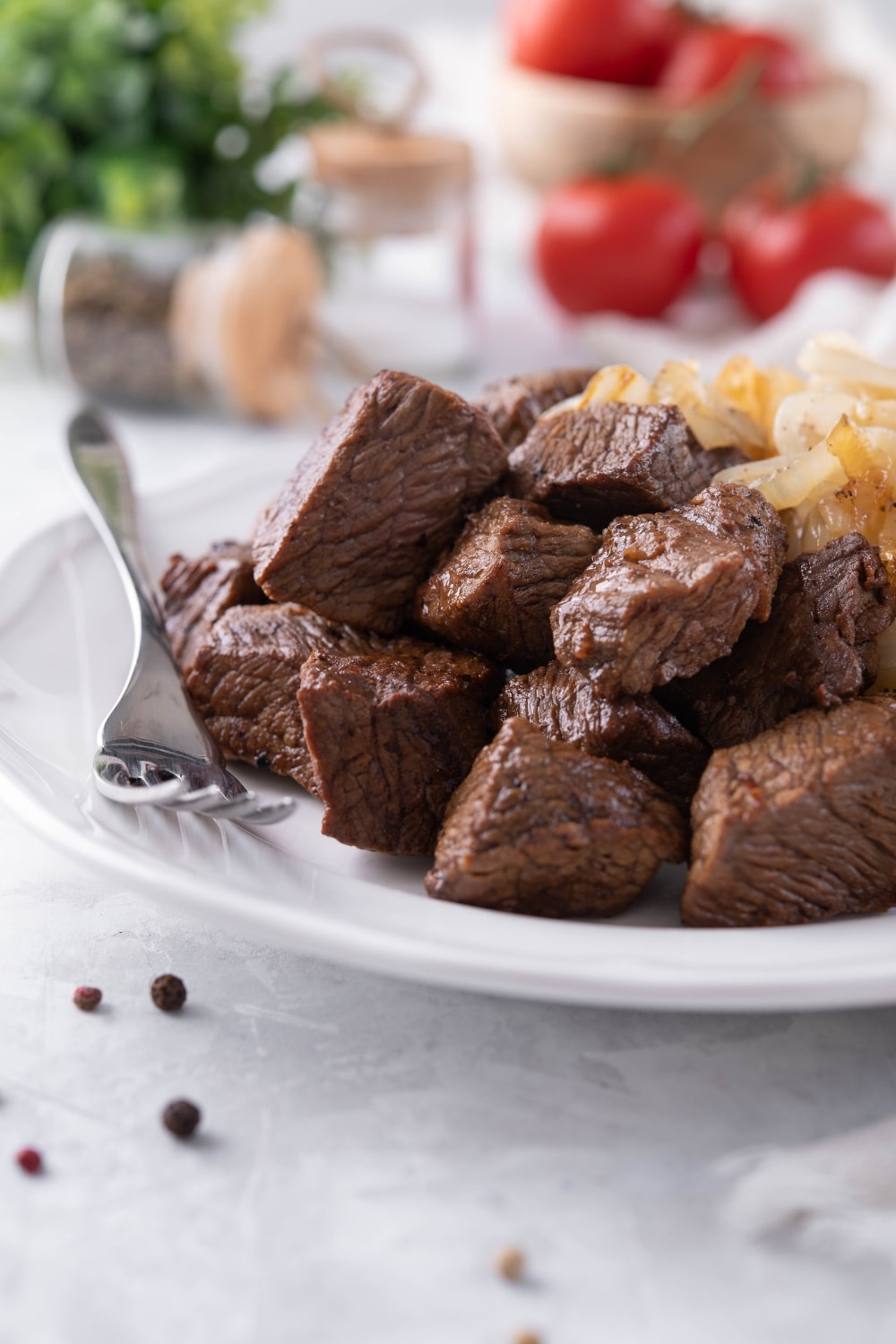 A plate of steak tips served with caramelized onions. A fork is resting on the plate.